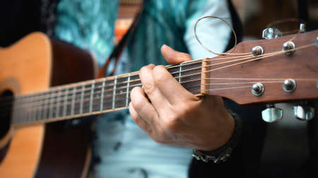 The young man plays hands and on a classic acoustic wooden guitar on the street using a microphoneの写真素材