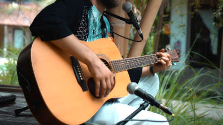 The young man plays hands and on a classic acoustic wooden guitar on the street using a microphoneの写真素材