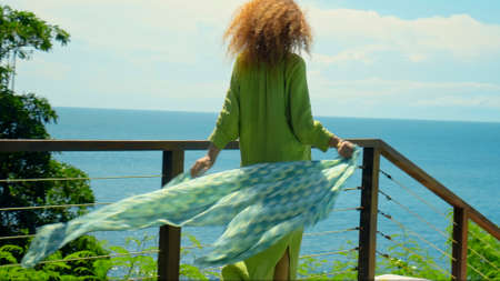 A young girl with red hair going on a grass in the backyard with a green garden in a beautiful long green dressの写真素材