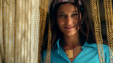 A young and beautiful European girl long-haired brunette stay in a room, looking into the camera and smiling touches a gold chain hanging with handsの写真素材