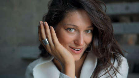 Young and beautiful European girl long-haired brunette sits at home on the stairs in autumn clothes and a white sweater and smiling touches herself with her handsの写真素材