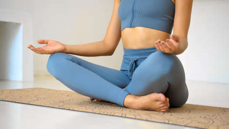 A young attractive European brunette girl makes a yoga in a white bright room on a yoga mat. Do sports at home alone.の写真素材