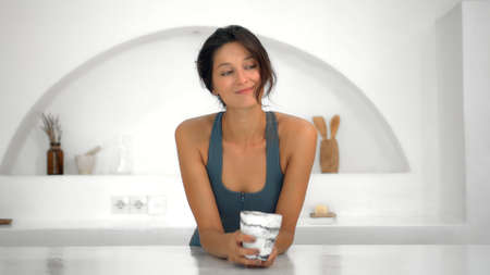 Young attractive European girl brunette drinks coffee and has cups holding it with both hands at home in a white bright roomの写真素材