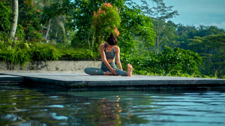 A young attractive European brunette sports girl makes yoga in nature with a green rainforest on a...