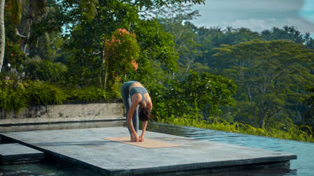 A young attractive European brunette sports girl makes yoga in nature with a green rainforest on a...