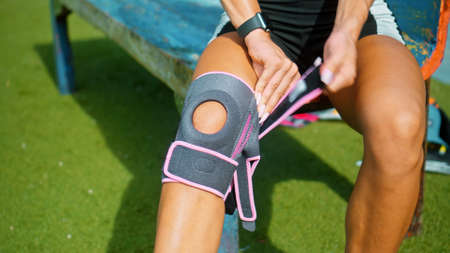 Young European girl athlete puts her hands on a protective band on her knee for sports with a knee injuryの写真素材