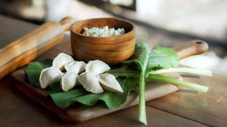 Traditional rustic Russian fresh handmade dumplings lying on a wooden table on a cutting board with cottage cheese in a wooden plate and spinachの写真素材
