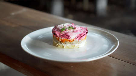 Traditional Russian fresh salad with beetroot and herring vegetables, lying on a wooden table in a white plateの写真素材