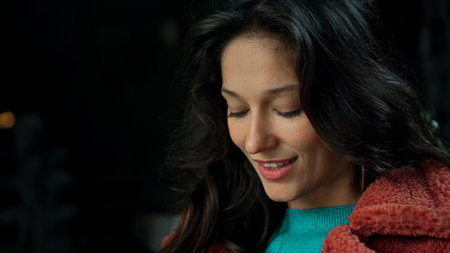 Young smiling European brunette girl in red coat and blue sweater stands and posing for camera