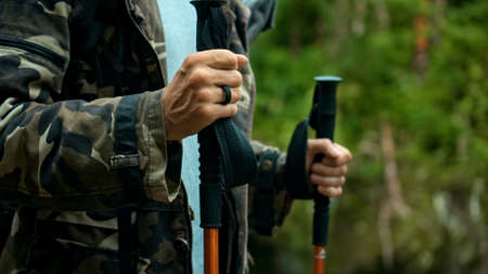 Hands of European young hiker hold rainforest walking sticks with green plants in backgroundの写真素材