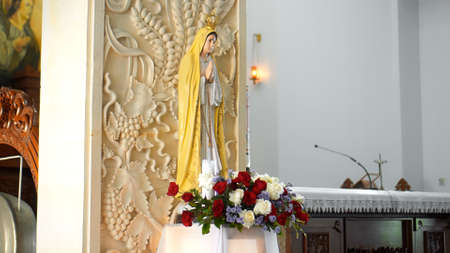 Statue of the Virgin Mary standing indoors with her head bowed looks straight