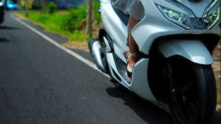 Legs of European girls in dresses driving the bike on a street on a road