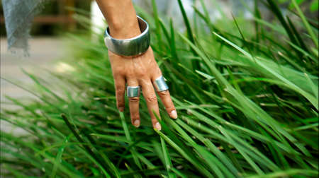 Young European girl's hand with rings and bracelet touches green growing grass