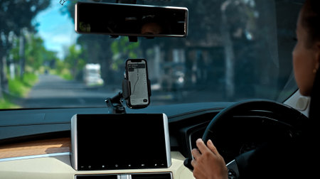 Hands of a young European girl sitting in a car with a black interior, touching the phone with her finger standing in the phone holder on the dashboard, a navigator map is shown on the screenの写真素材