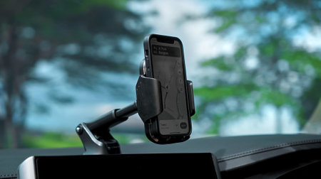 Hands of a young European girl sitting in a car with a black interior, touching the phone with her finger standing in the phone holder on the dashboard, a navigator map is shown on the screenの写真素材