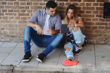 Young beautiful couple sitting outdoors using tabletの写真素材