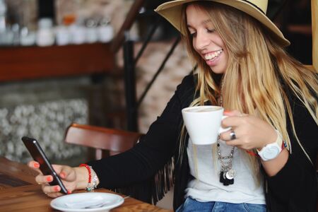 Young beautiful woman using her smartphone and drinking coffe sitting on urban cafeの写真素材