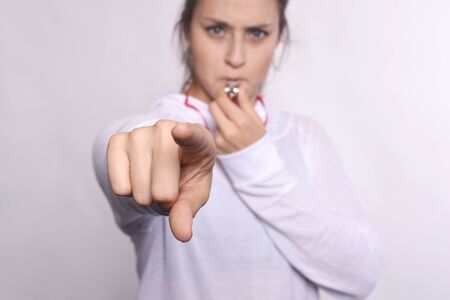 Portrait of young beautiful woman with whistle and pointing camera. Isolated white background.
