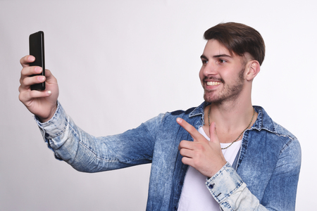 Portrait of attractive young man taking a selfie with his smartphone. Isolated white background.の写真素材