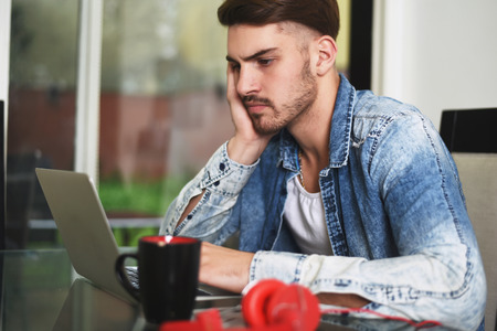Young handsome man studying with his laptop, headphones and coffee. Indoor.の写真素材