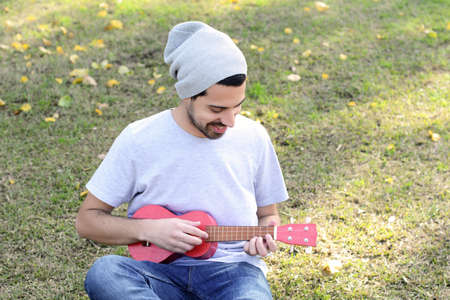 Portrait of young handsome man playing the ukelele in a park. Outdoors.