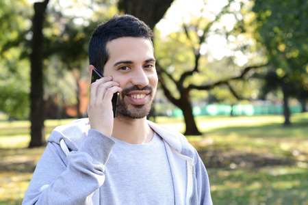 Portrait of young handsome man talking on the phone in a park. Outdoors.