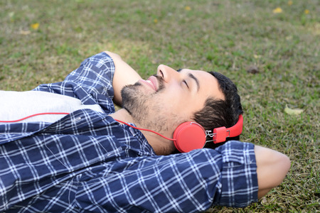 Young attractive man listening to music with red headphones in a park. Outdoors.の写真素材