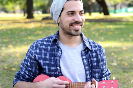 Portrait of young handsome man playing the ukelele in a park. Outdoors.の写真素材
