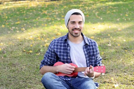 Portrait of young handsome man playing the ukelele in a park. Outdoors.の写真素材