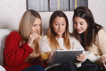Portrait of three and beautiful young friends having fun and using tablet. Indoors.の写真素材