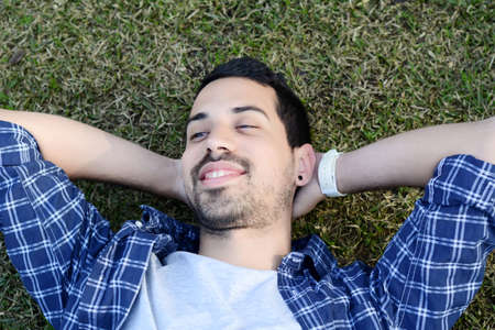 Young latin man relaxing lying on the grass. Outdoors.の写真素材