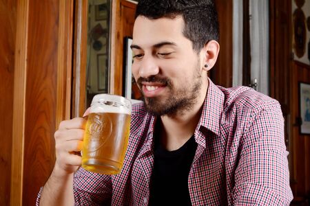 Portrait of young latin man drinking beer at a bar. Indoors.