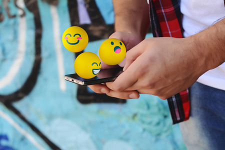 Young latin man using smartphone sending emojis. Social concept.