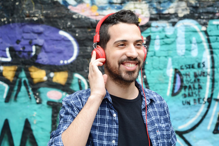 Portrait of young latin man with red headphones. Urban scene.