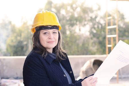 Portrait of a beautiful female architect at a construction site with blueprints. Outdoors.の写真素材