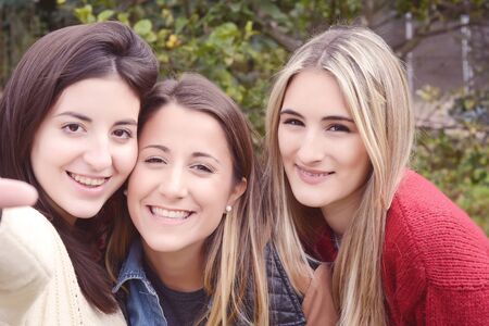 Portrait of three and beautiful young friends having fun and taking selfie. Outdoors.の写真素材