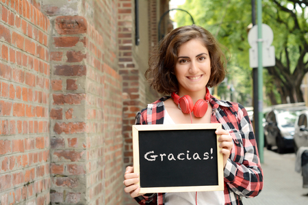 Young beautiful woman holding chalkboard with text "Gracias". Outdoors.の写真素材
