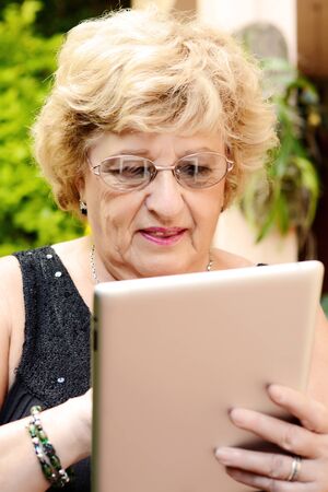 Portrait of an elderly woman using digital tablet. Outdoors.
