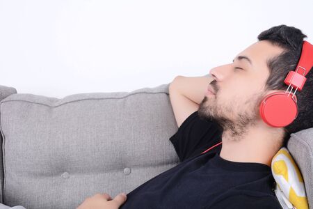 Attractive young man listening to music with headphones and relaxed on couch. Indoors.の写真素材