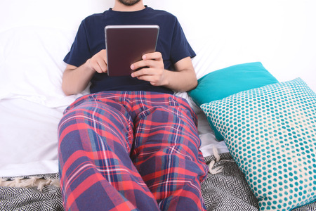 Attractive young man using digital tablet and relaxed on bed. Indoors.の写真素材