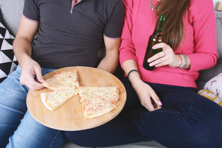 Beautiful young couple drinking beer and eating pizza. Indoors.の写真素材
