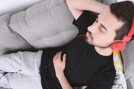 Attractive young man listening to music with headphones and relaxed on couch. Indoors.の写真素材