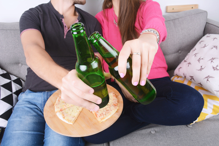 Beautiful young couple drinking beer and eating pizza. Indoors.の写真素材