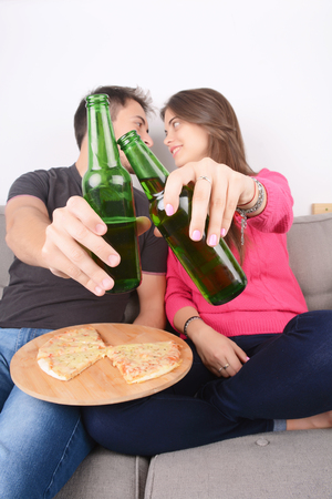 Beautiful young couple drinking beer and eating pizza. Indoors.の写真素材