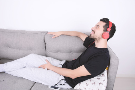 Attractive young man listening to music with headphones and relaxed on couch. Indoors.の写真素材