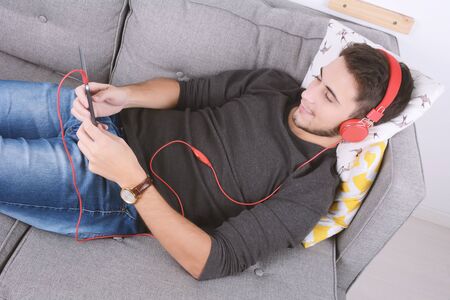 Attractive young man listening to music with digital tablet on couch. Indoors.の写真素材