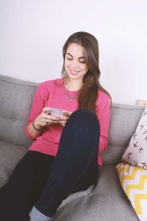Beautiful young woman using her smartphone and relaxed. Indoors.の写真素材
