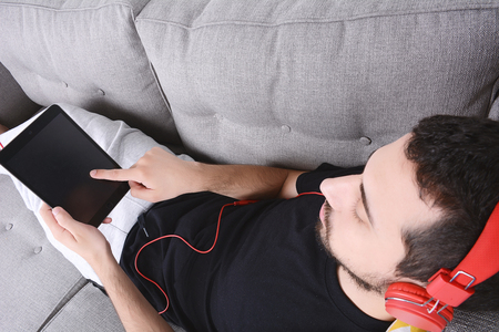 Attractive young man listening to music with digital tablet on couch. Indoors.の写真素材