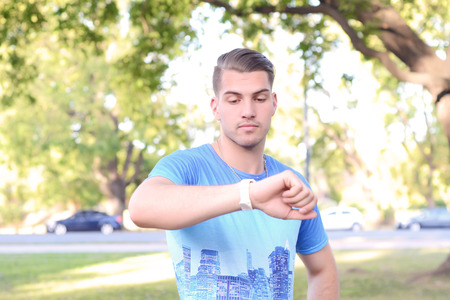 Portrait of young latin man looking at his watch at park. Outdoors.