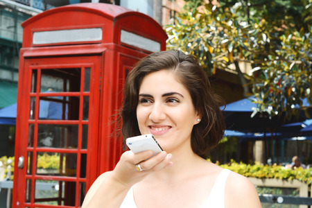 Portrait of a young beautiful woman sending voice messages. Outdoors.の写真素材